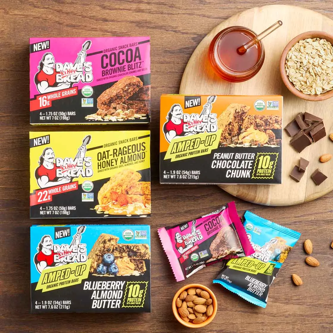 Dave's Killer Bread snack bars arranged on a wooden table with honey, oats, and almonds
