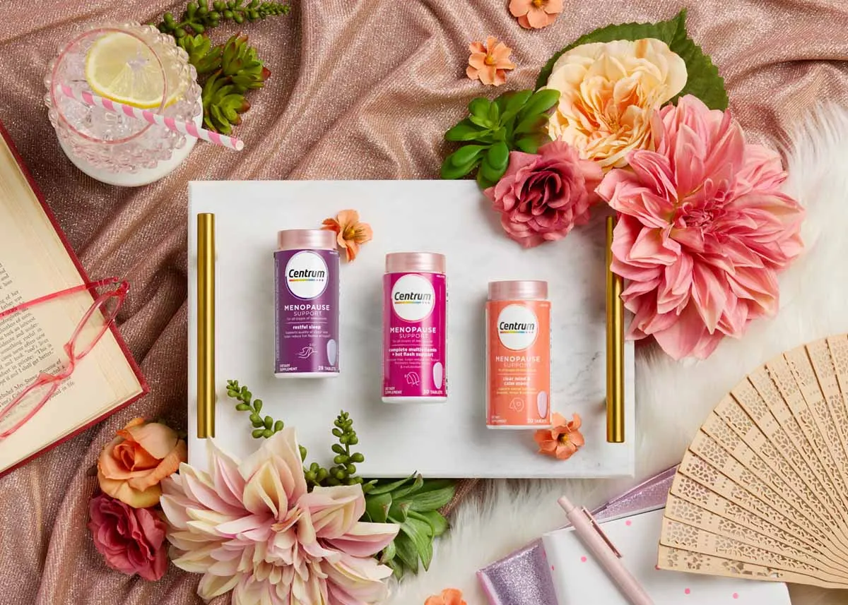 Three Centrum supplement canisters on a marble tray surrounded by dahlias and a paper fan