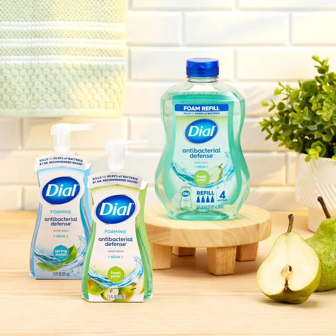 Dial foaming hand soap and refill bottle on a bathroom counter beside a pear