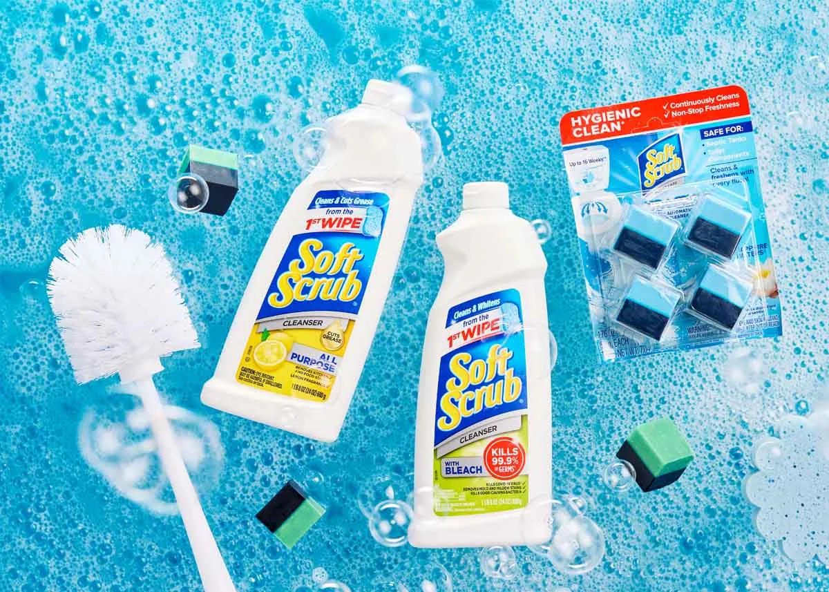 Soft Scrub cleaners and a toilet brush floating on bright blue soapy water