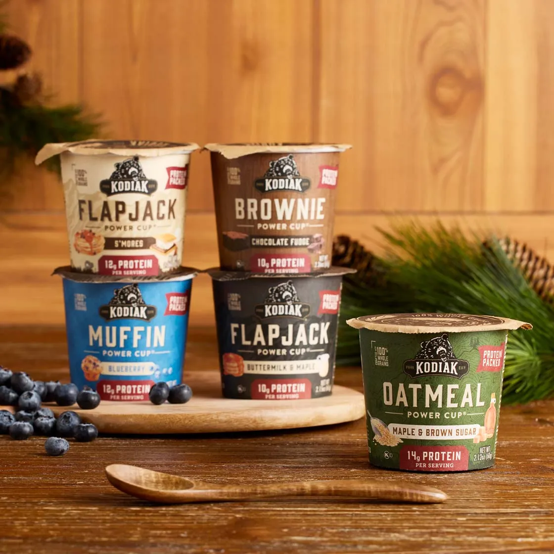 Kodiak power cups stacked on a wooden board with blueberries and pine branches