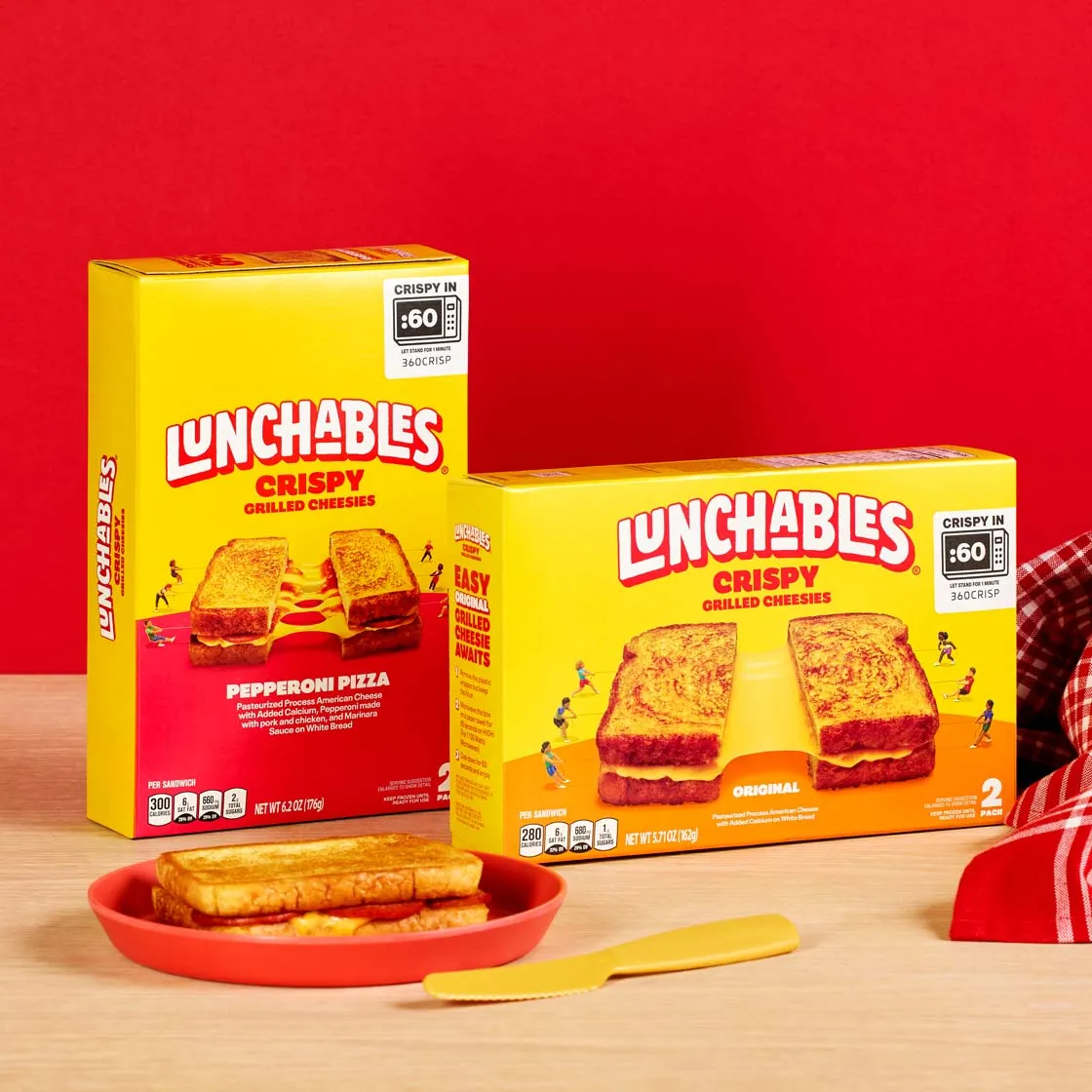 Lunchables Crispy Grilled Cheese boxes against a red wall with a plate of sandwiches