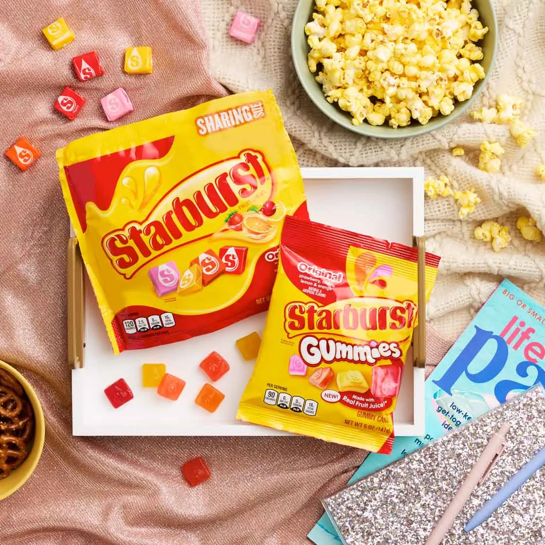 Starburst candy and gummies on a cozy blanket with popcorn and a board game