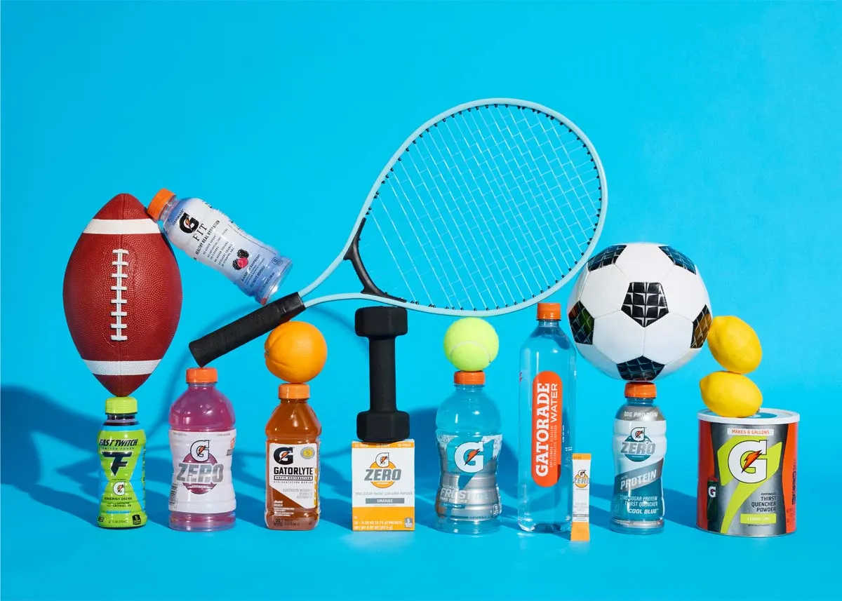 Gatorade bottles lined up with sports balls and a tennis racket on a blue backdrop