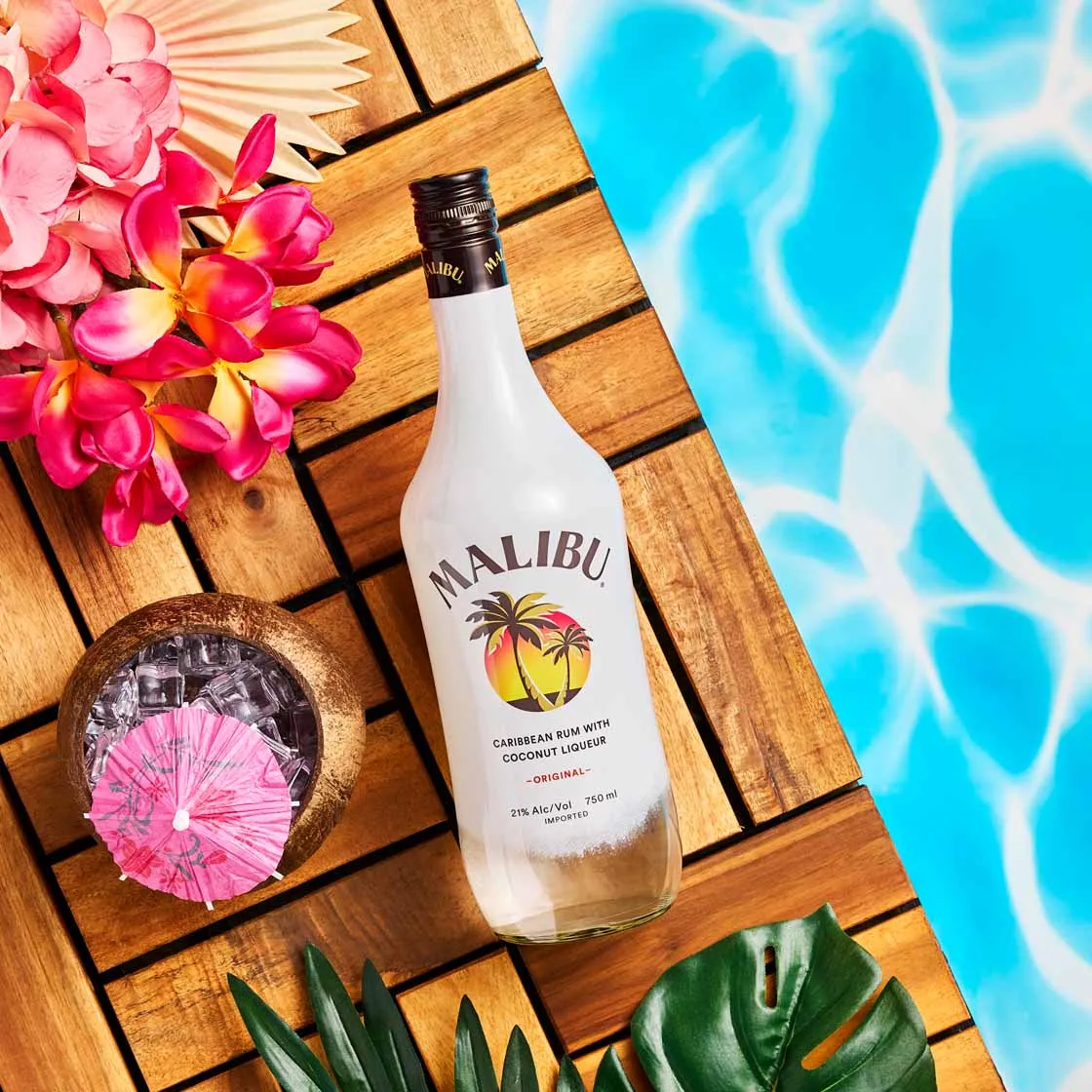 Malibu rum bottle on a poolside deck with tropical flowers and a cocktail