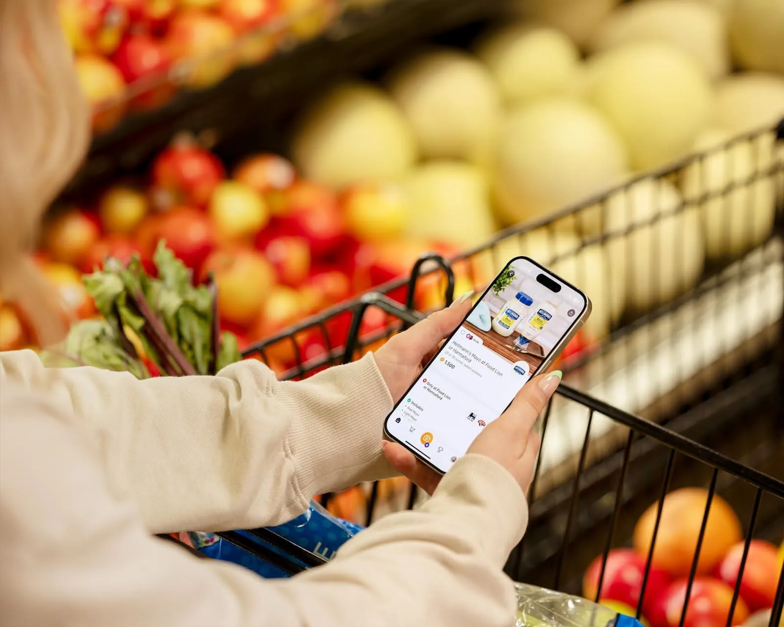 Shopper checking a phone app over a cart of fresh produce