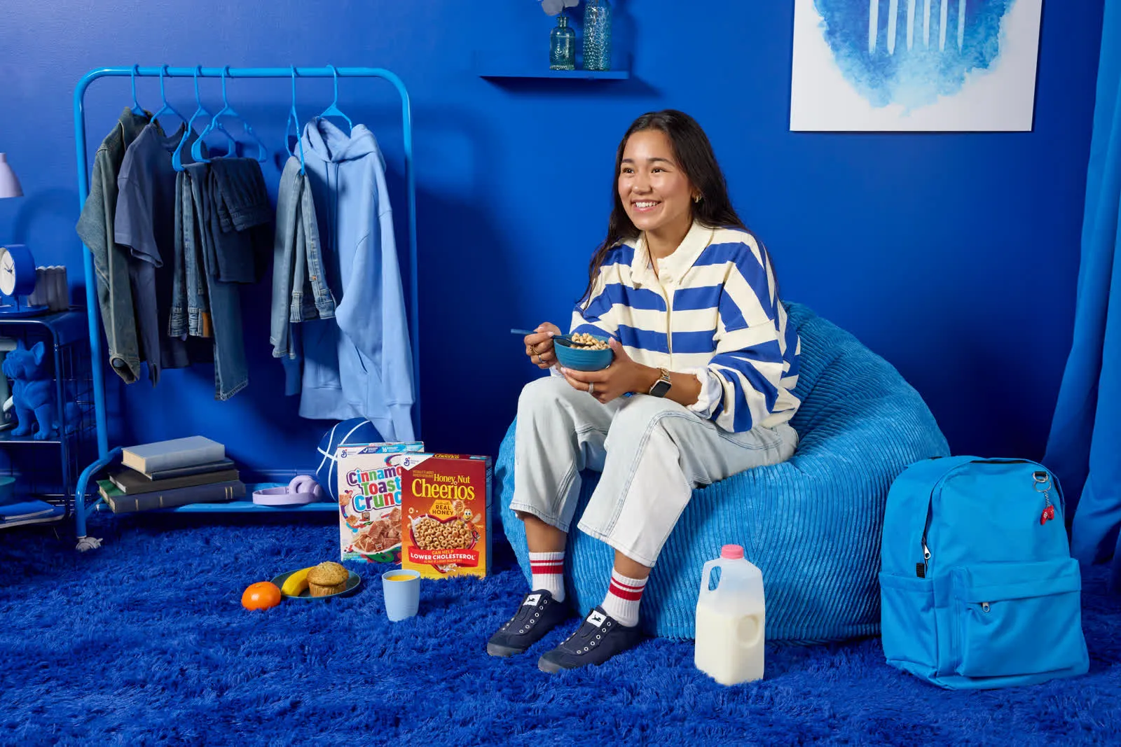 Student sitting on a blue bean bag in a dorm room with cereal and snacks