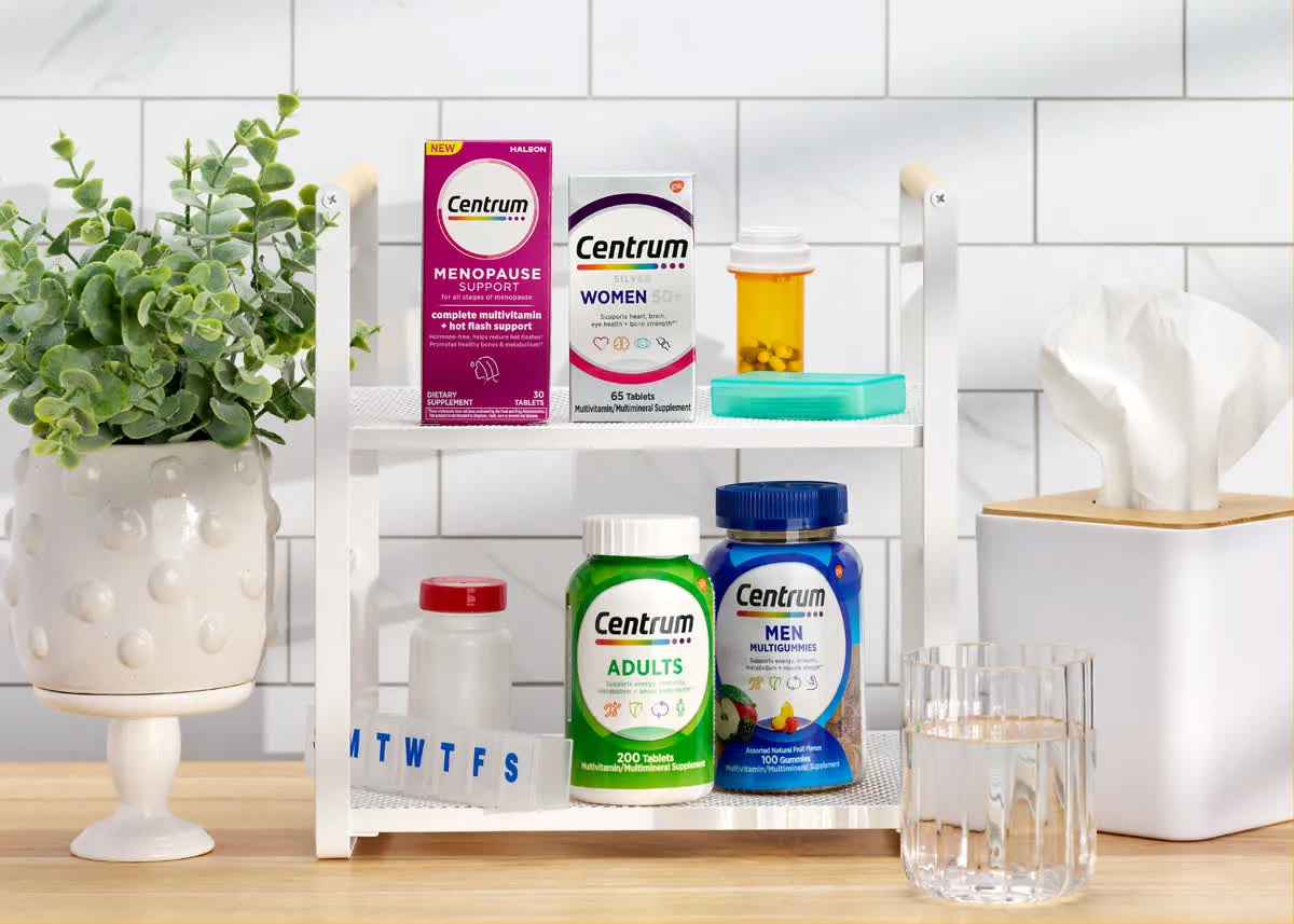 Centrum vitamins on a white shelf beside a plant and tissues